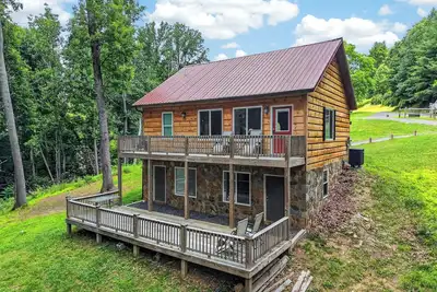 Image de A secluded, multi-level log cabin featuring a spacious wooden deck, open-concept living, a fully equipped modern kitchen, and comfortable sports-themed bunk rooms.