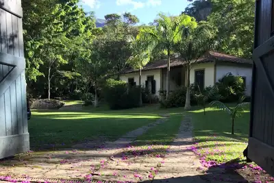 Image de maison coloniale avec deux autres petites maisons sur le bord d'une rivière et le long de la forêt.