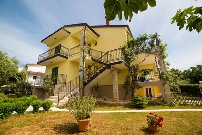 Maison avec jardin, en face se trouve un parc verdoyant avec des jouets.