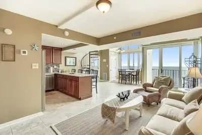 Image de Activites Quotidiennes Gratuites! Oceanfront penthouse sur deux niveaux. Joliment meublé avec des canapés rembourrés avec chaise en osier et pouf dans le salon.