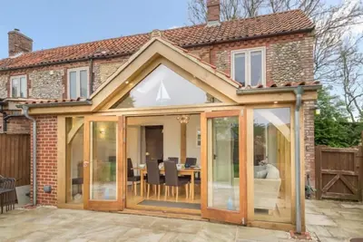 Image de Un chalet traditionnel en brique et silex, récemment rénové pour offrir un hébergement moderne pouvant accueillir jusqu'à six personnes. Le chalet est joliment présenté, avec l’ajout fantastique d��une salle de jardin avec cadre en chêne menant au jard.