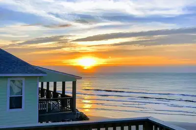 Martinis & Bikinis, a beach front house with toes in the sand drink in the hand.